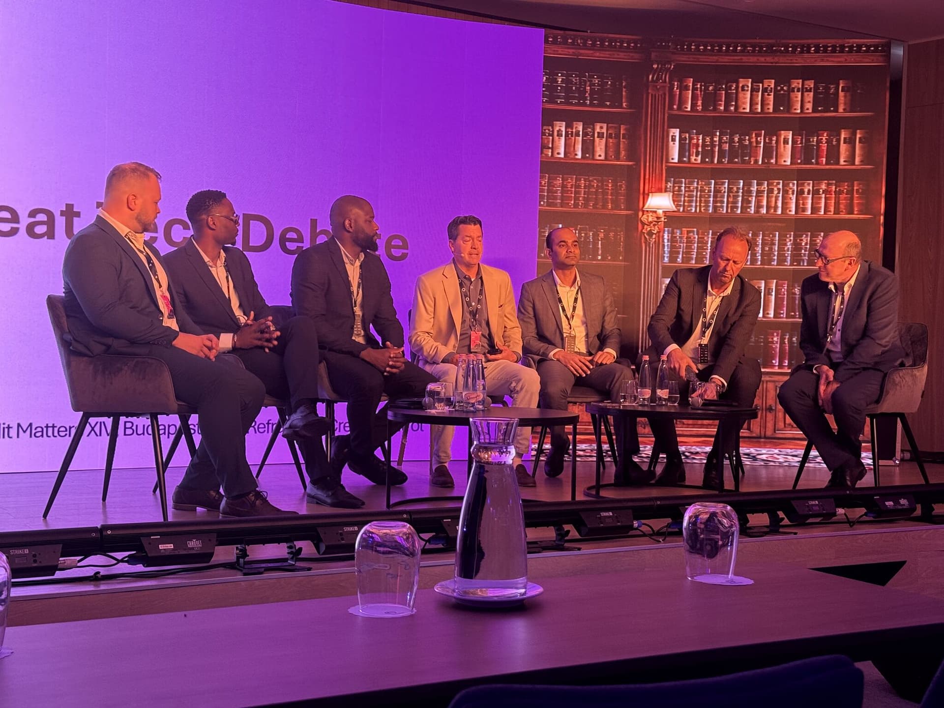 The Great Tech Debate — seven panellists under purple stage light